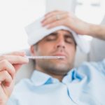 Sick man lying on sofa checking his temperature